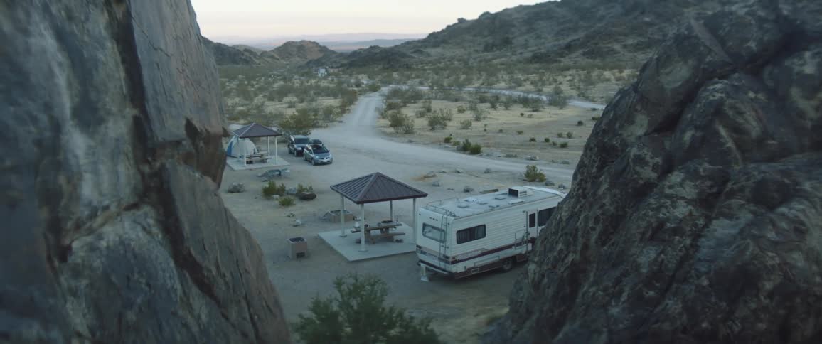 A camper and tent are set up below a canyon
