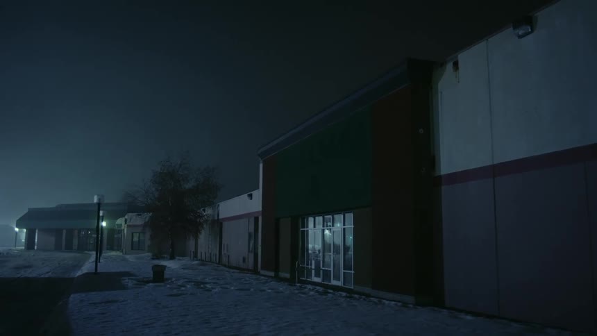 Streetlights shine in distance of abandoned mall with snowy walkway at night