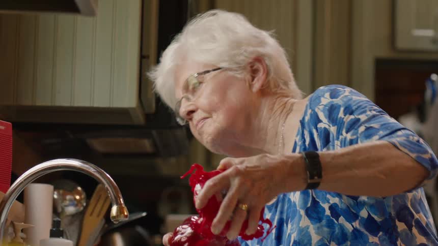 A elderly woman look out her window filling a bird feeder