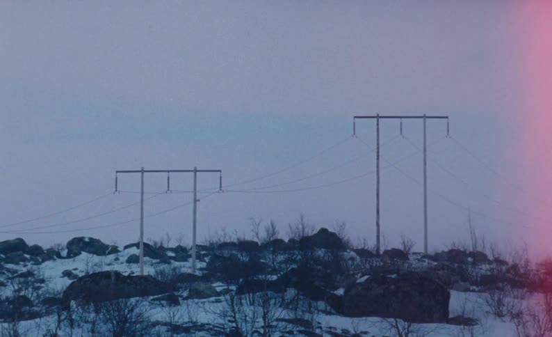 Poles carry power lines along snow covered and boulder strewn hill