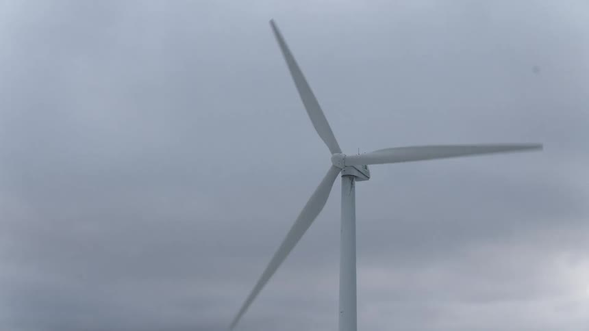 Blades on wind turbine rotate slowly under an overcast sky