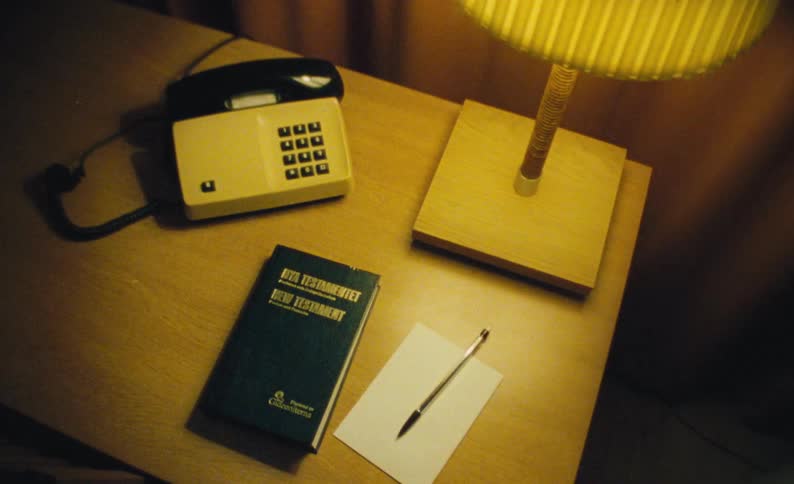 A telephone on a desk next to lamp booklet and paper and pen