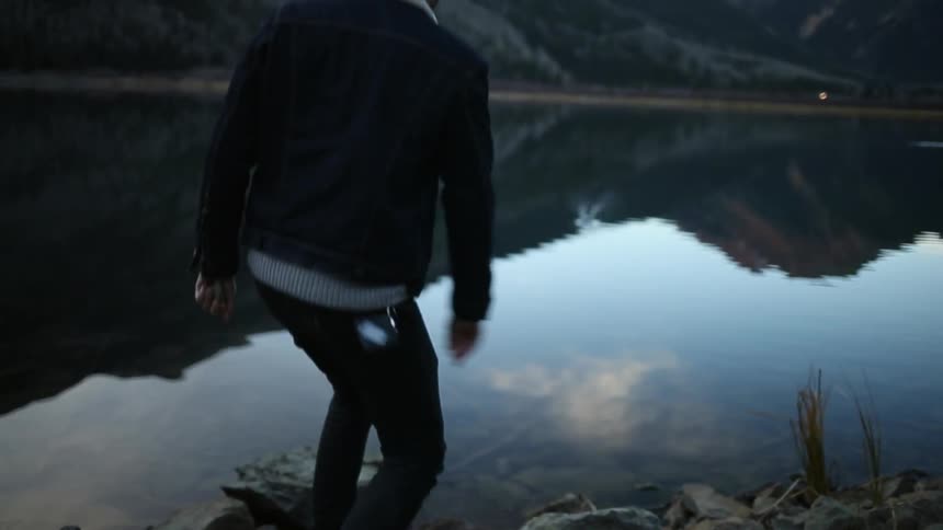 A man skips a rock on a mountain lake on an overcast, cold day
