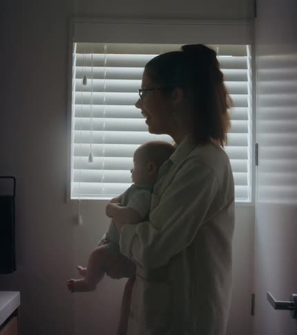 A woman is standing in a room holding her baby as she smiles and talks