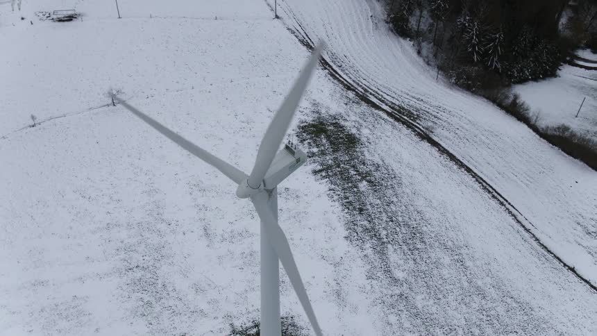 A wind turbine spins in a snowy field