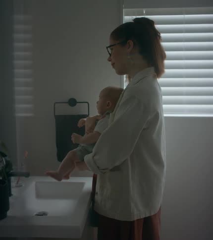 A woman rocks a baby in her arms while standing before a bathroom mirror