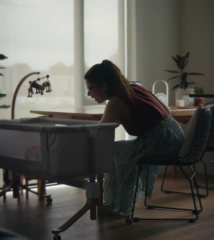 A woman turns to check on her baby while working on her laptop at home