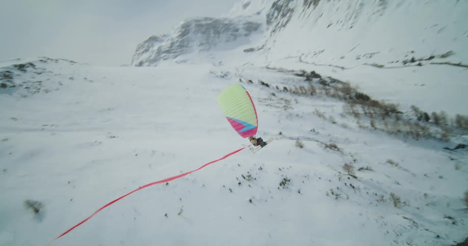 Speedriding paraglider flies over snow covered mountains trailing a long red ribbon