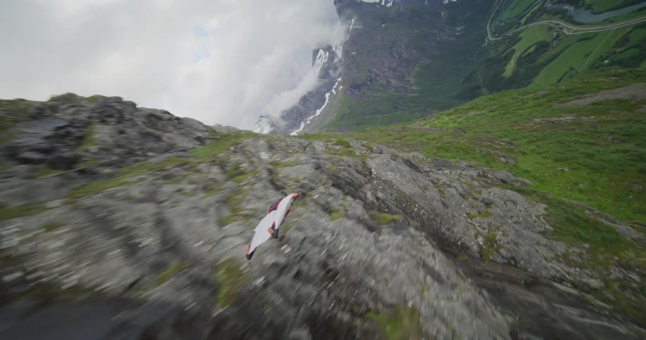 A person in a white suit gliding over rocky mountain ranges and then green grasslands