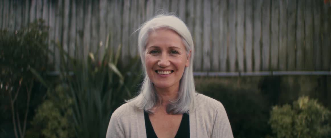 A woman is smiling outdoors in her garden