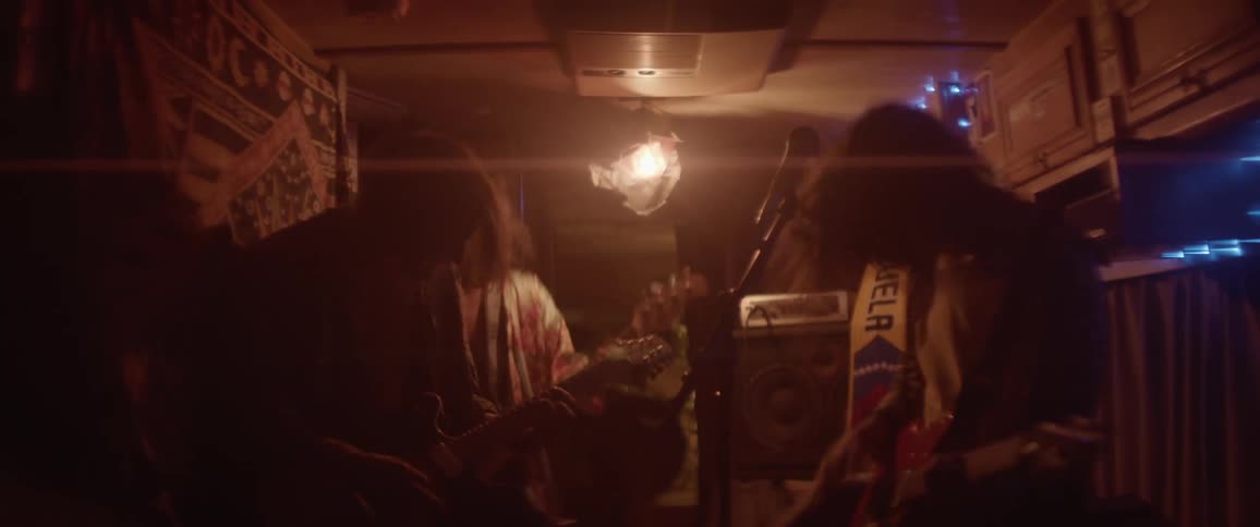 A band jumps up and down while playing guitars in an RV
