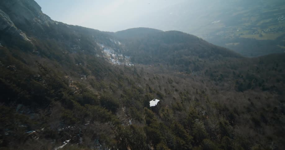 A person jumping off a cliff and gliding in a suit through mountains