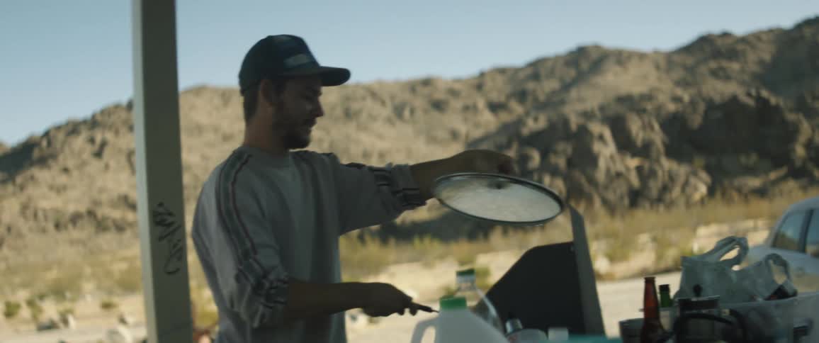 A man cooking on a cooktop outside while holding a glass top