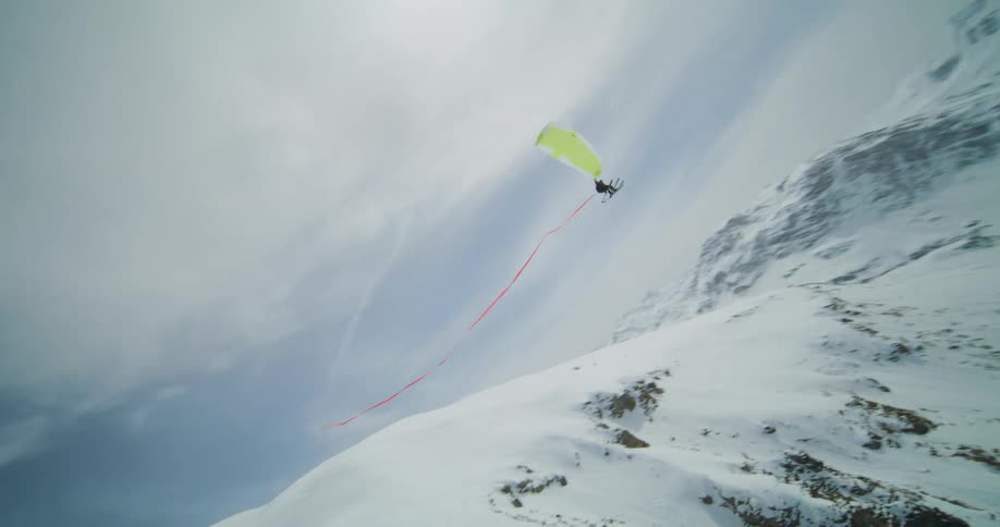 A person wearing skis is paragliding down the side of a snow covered mountain as a long red ribbon follows behind them