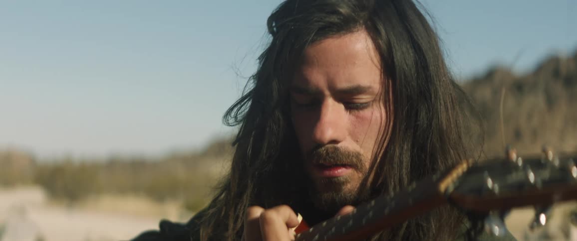 Guitarist plays instrument in arid area near rocky hills