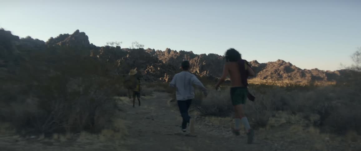 A group of friends run down a desert trail at sunset
