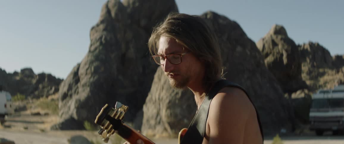 Man playing a guitar in front of vehicles