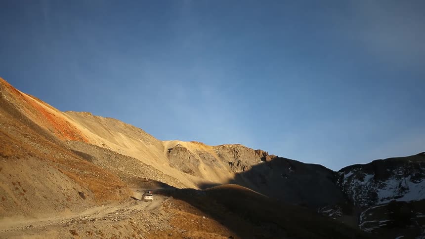 A car is traveling along a small road near hills