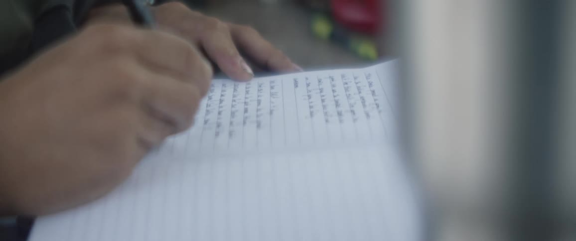 A person uses a pen to write in a notebook at an outdoor table