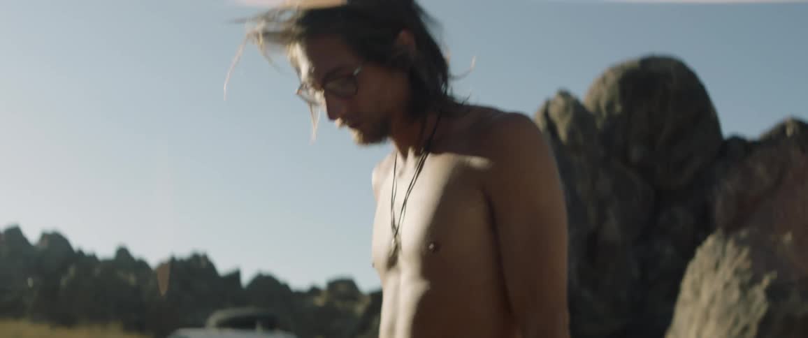 A shirtless man playing air guitar outside on a sunny day