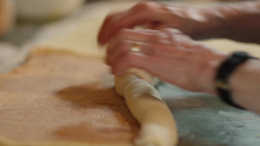 A persons hands rolling cinnamon covered dough on a surface