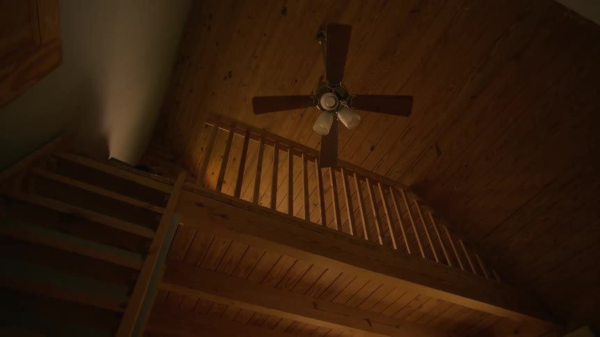 A wood ceiling and railing on a loft area with a ceiling fan and light on the ceiling