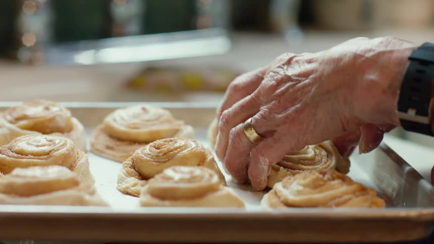 An elderly person arranging cinnamon rolls on a baking sheet