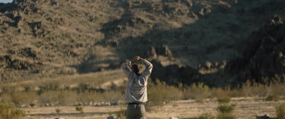 A man stretches and looks out at a mountain in the desert