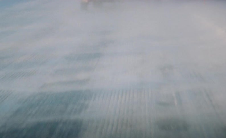 A vehicle drives across a road with blowing snow