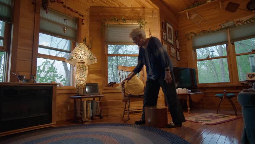 Elderly woman with glasses sits down in armchair in the living room