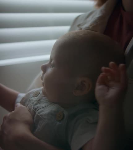 A baby doing baby things while being held by their mother