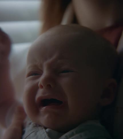 A baby crying in and adults arms near a window