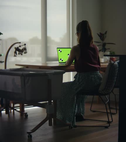 Woman with brown hair and glasses sits at table working on tablet in room