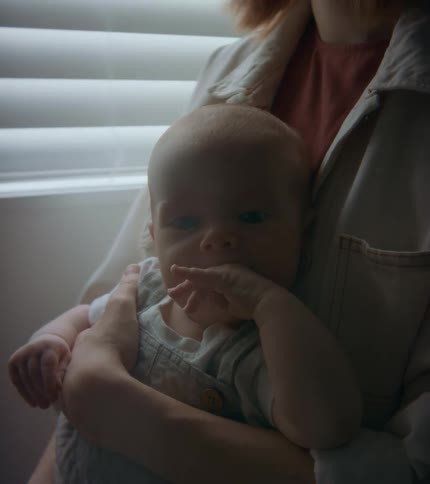 A woman is holding her baby as they smile and move their hand