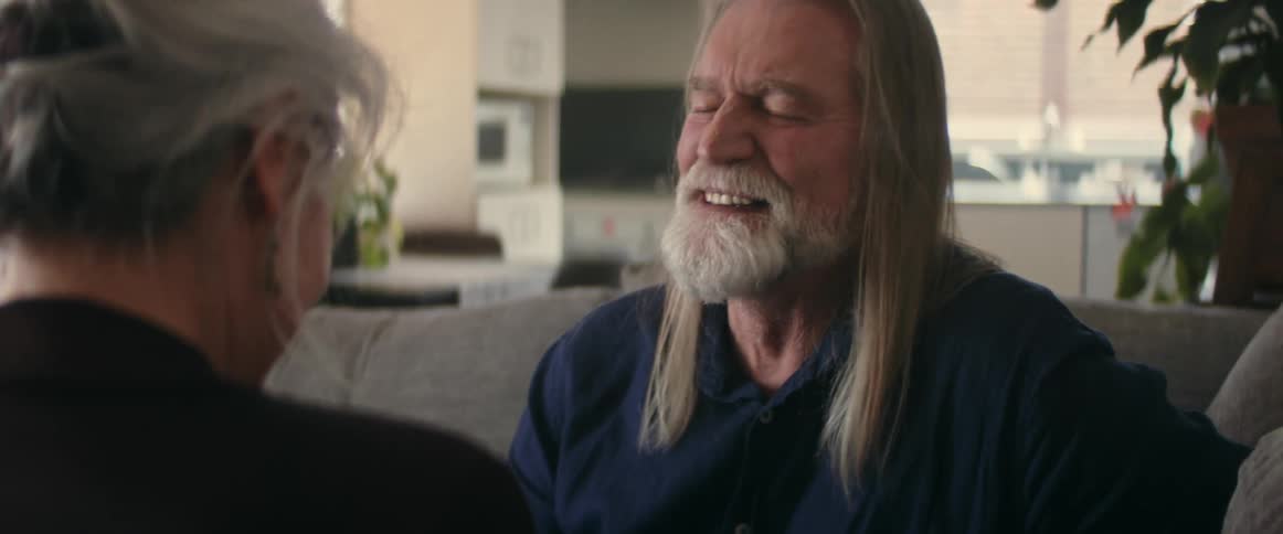 An elderly man and woman smiling and laughing while talking at home