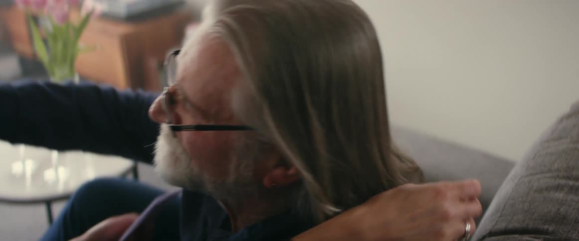 Elderly man with gray hair glasses and beard and woman with gray hair hold and cuddle each other in the living room