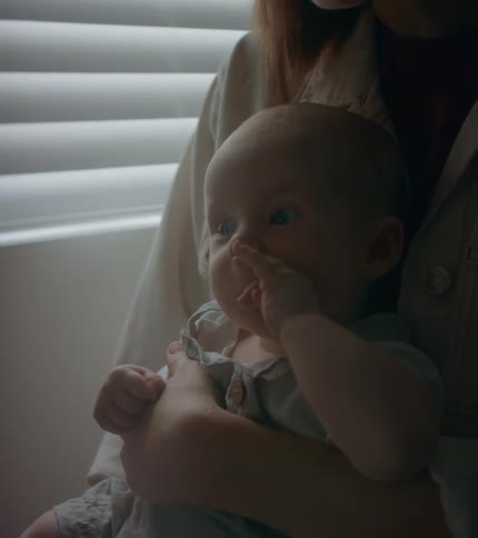 A woman sits at home and holds her infant son in her lap