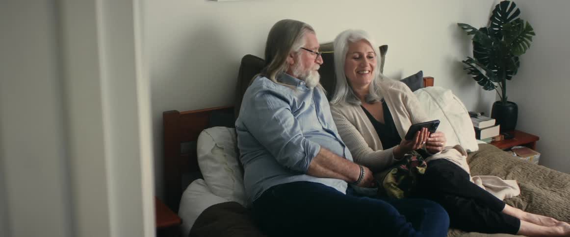 An elderly couple is sitting together and looking at a cell phone