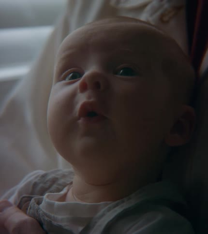 A baby is sitting with there mom and looking at the camera