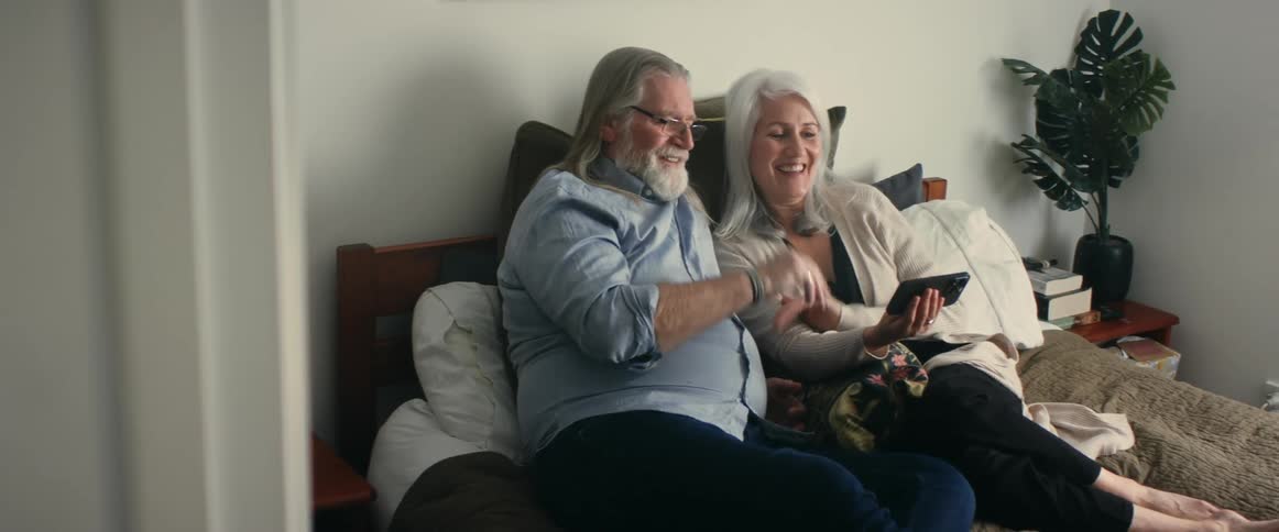 A man and woman looking at a phone smiling and waving