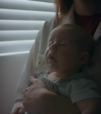 An infant sneezes while his mother holds him