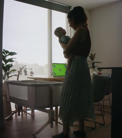 A mother is walking toward a wooden desk while cuddling a baby