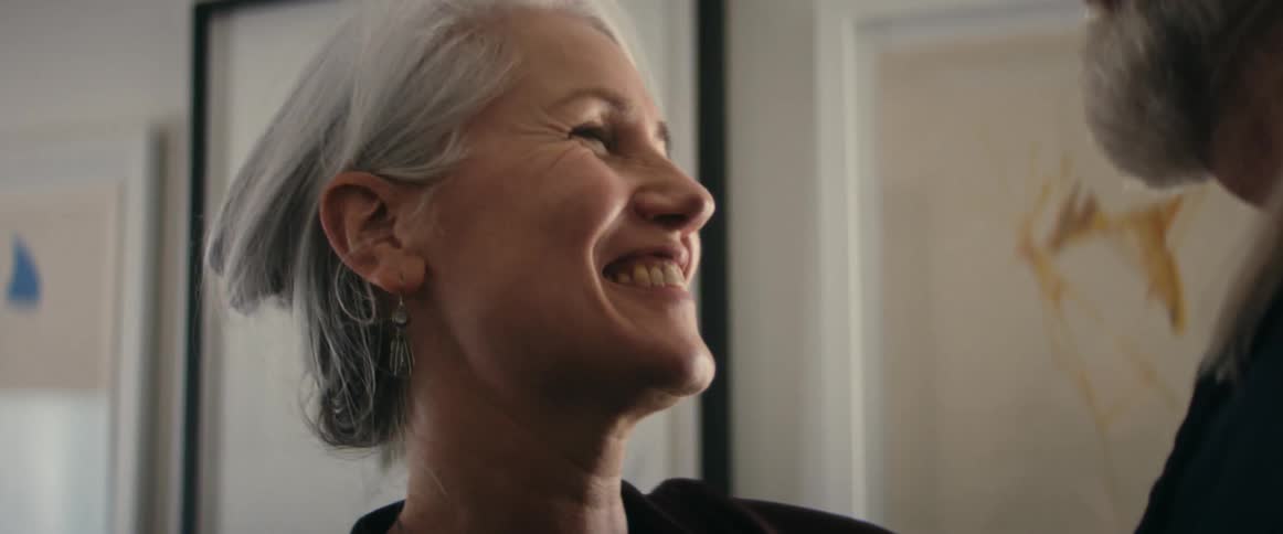 Woman with gray hair earrings and brown shirt dances with elderly man with beard smiling at each other