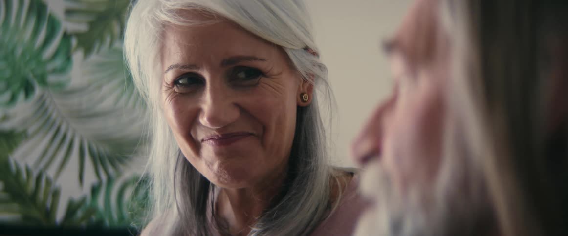 An up close of a mans face while he is talking and smiling to a women with grey hair who is smiling back