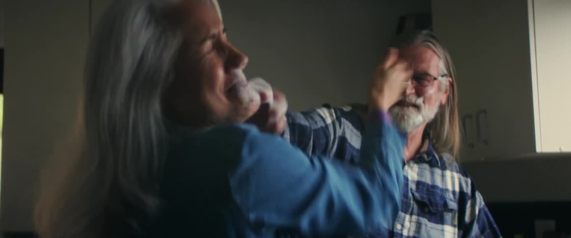A man and woman playfully put something on each others face smiling and laughing