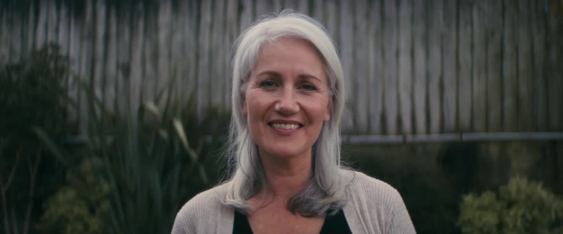 A woman with grey hair stands smiling at the camera