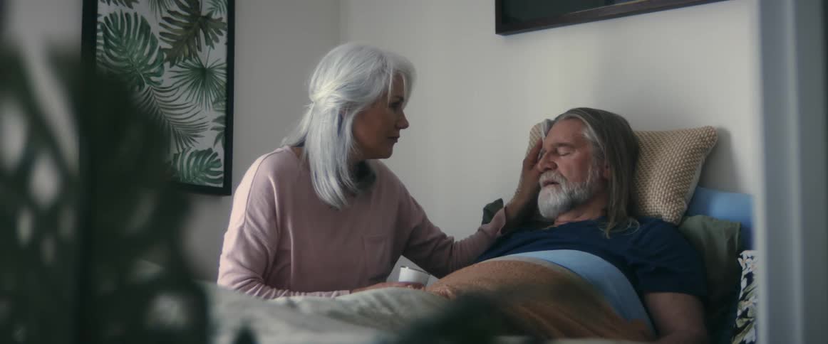A woman helps a bedridden man take his medicine