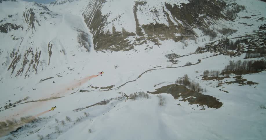 Two gliders in yellow suits sailing through a snowy valley