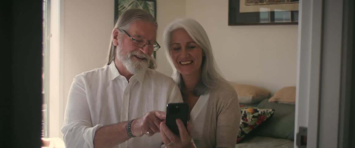 A man and a woman smiling together looking at a cellphone while the man points at it