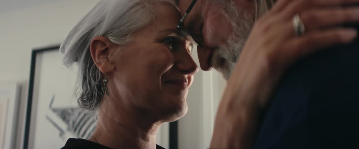 Older couple smile andtouch foreheads while slow dancing in home
